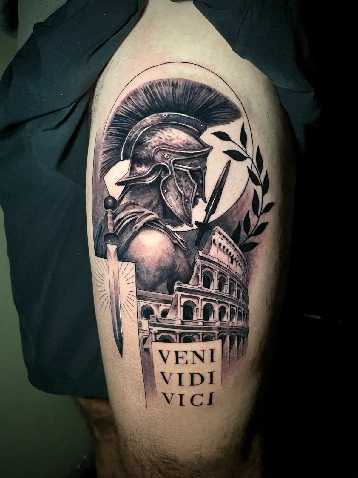 Black and grey realism Roman gladiator with Colosseum and Veni Vidi Vici lettering tattoo on upper arm by Paul Michael Andras