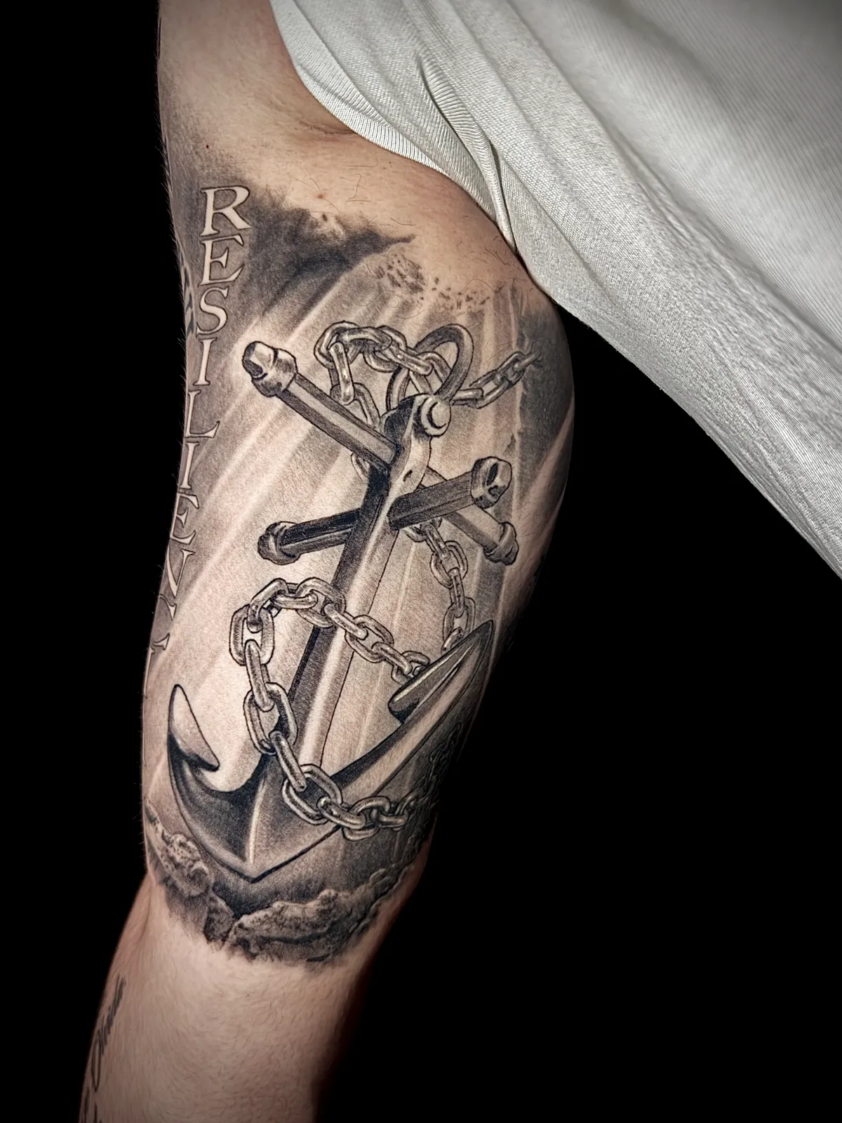 Black and grey realism anchor with chain and Resilience lettering inner bicep tattoo by Paul Michael Andras