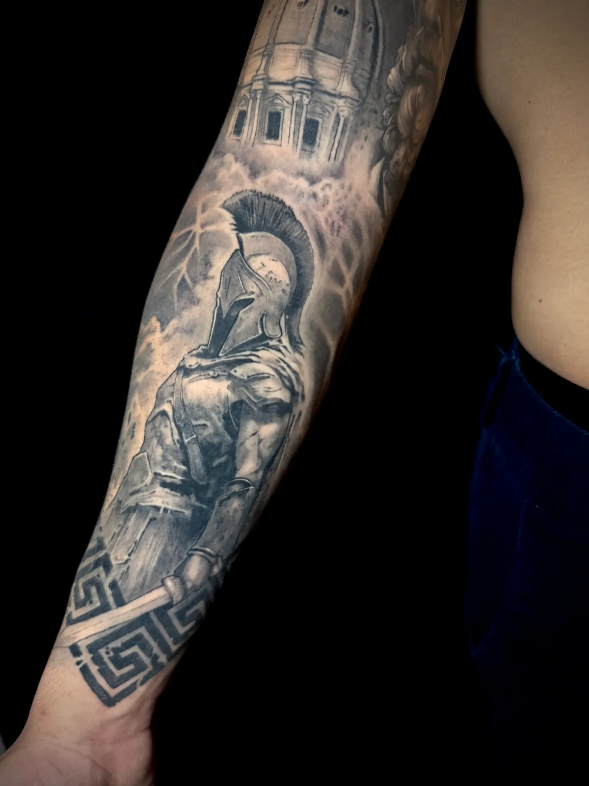 Black and grey realism Spartan warrior with temple and Greek key border forearm sleeve tattoo by Paul Michael Andras