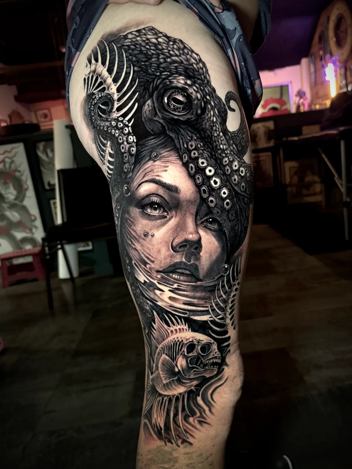 Black and grey realism woman portrait with octopus and skeletal fish large scale thigh tattoo by Andras Tattoo