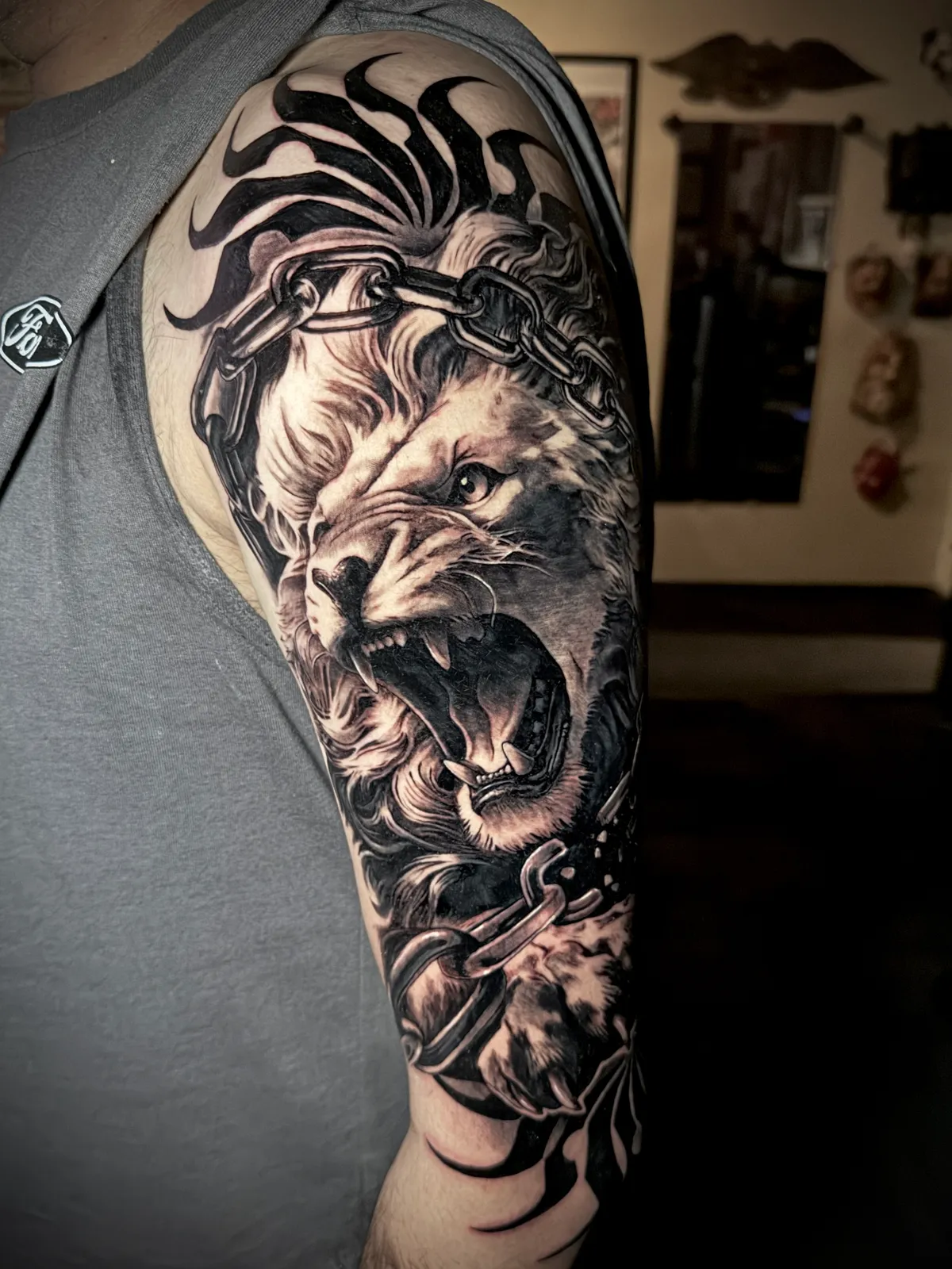 Black and grey realism roaring lion with chains and crown detail large scale upper arm tattoo by Andras Tattoo