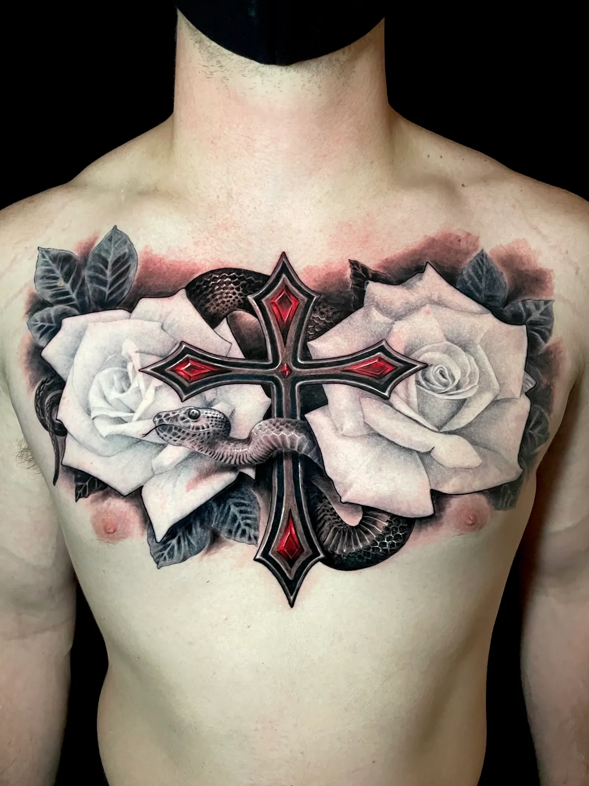Black and grey realism ornate cross with roses and snake chest piece tattoo with red gem accents by Paul Michael Andras